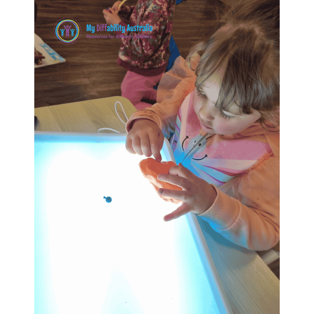 Messy Play Light Box with young girl playing orange putty on top