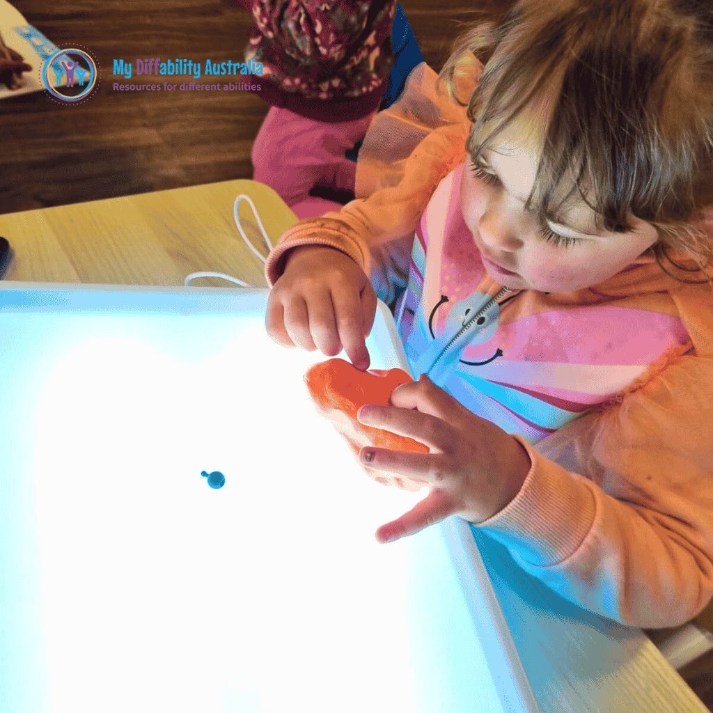 picture showing messy play light box wherein kid is playing orange putty on top of it